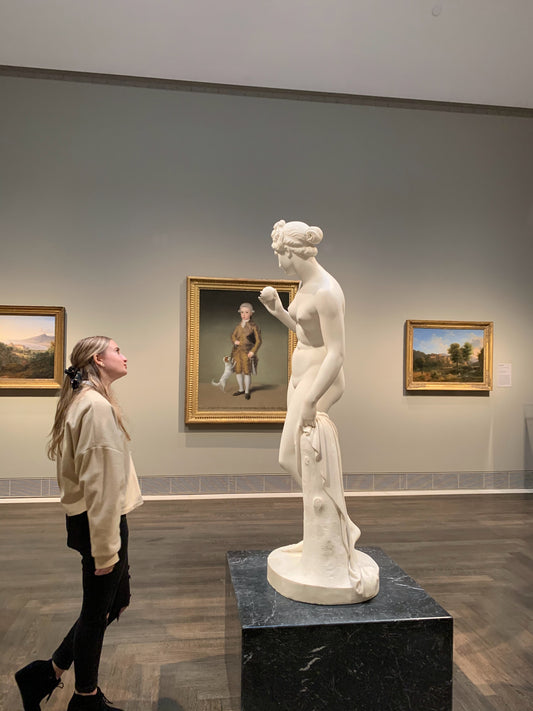 Woman in beige coat viewing a statue. Photo by Karlie Mitchell for Unsplash